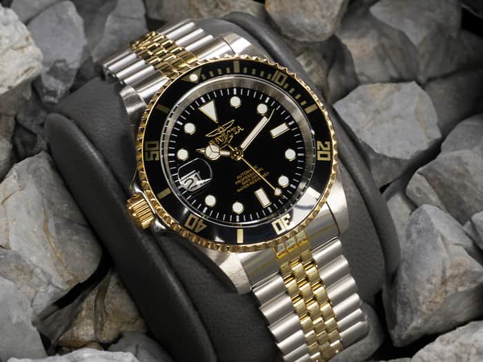 Image of a silver wristwatch with golden details, with a black clock face and white hour markers.