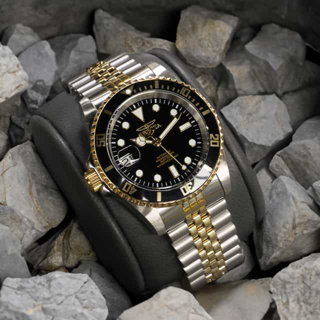 Image of a silver wristwatch with golden details, with a black clock face and white hour markers.