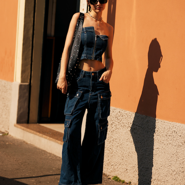 young female wearing a denim co ord outfit in a festival style, standing in front of an orange wall