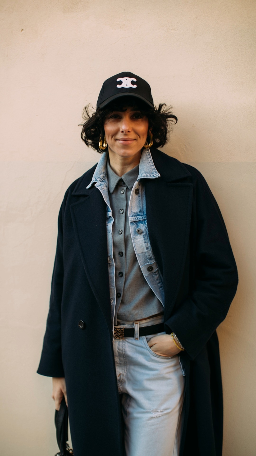 A woman wearing a stylish outfit with layering items consisting of a long blue wool trench coat, a light blue wash denim jacket and a grey shirt for a base layer. 