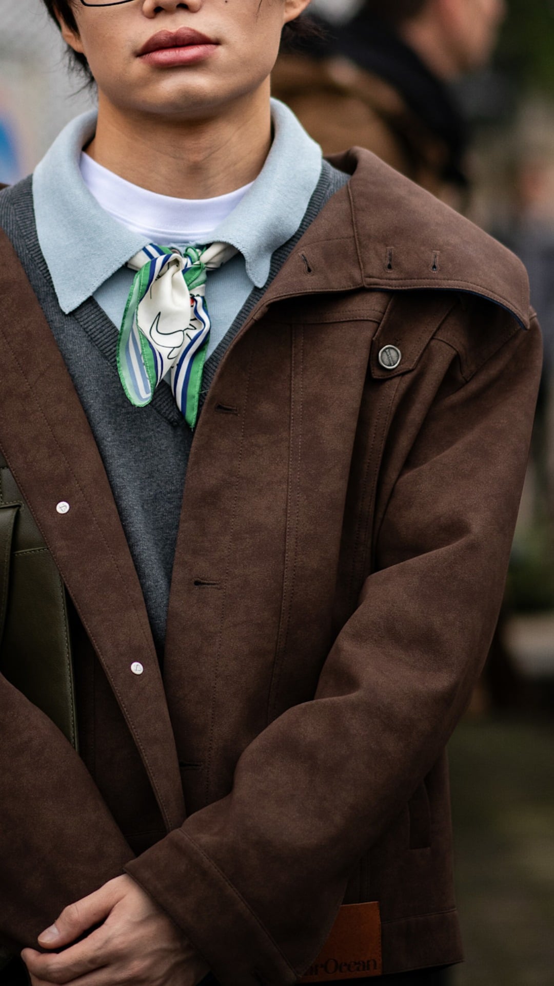 A man with multiple layered collars on show from a brown suede jacket, a light grey knitted polo shirt, a tshirt and e neck scarf